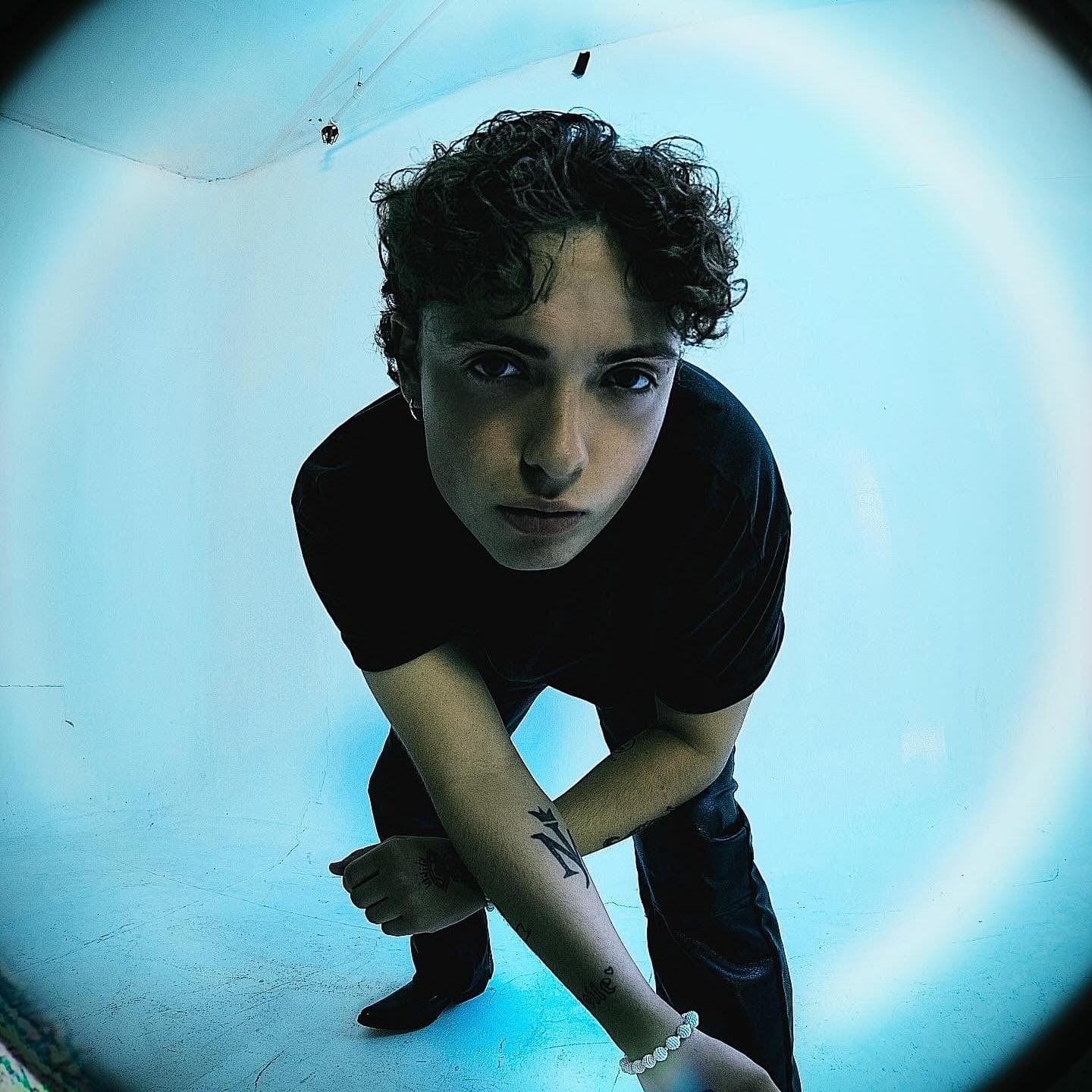 Jonathan on a blue background looking at the camera, taken with a fish-eye lense